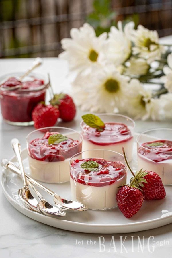 Tray of individual serving cups with panna cotta topped with strawberry sauce and mint at a party.