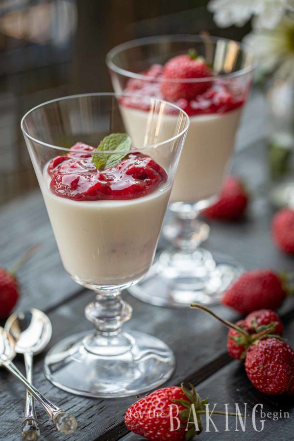 Two wine glasses filled with panna cotta and topped with strawberry sauce and a mint leaf. 