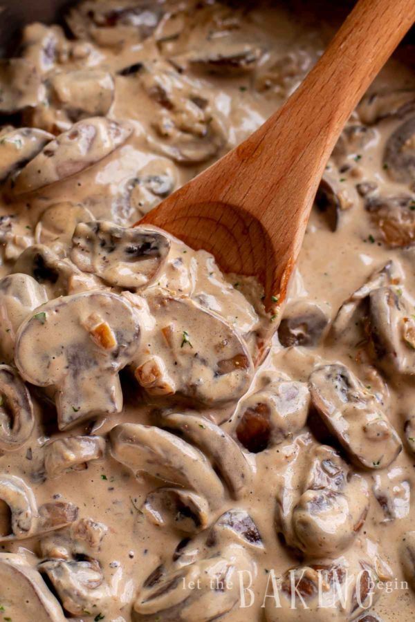 Creamy mushroom sauce being stirred in a pot with a wooden spoon.