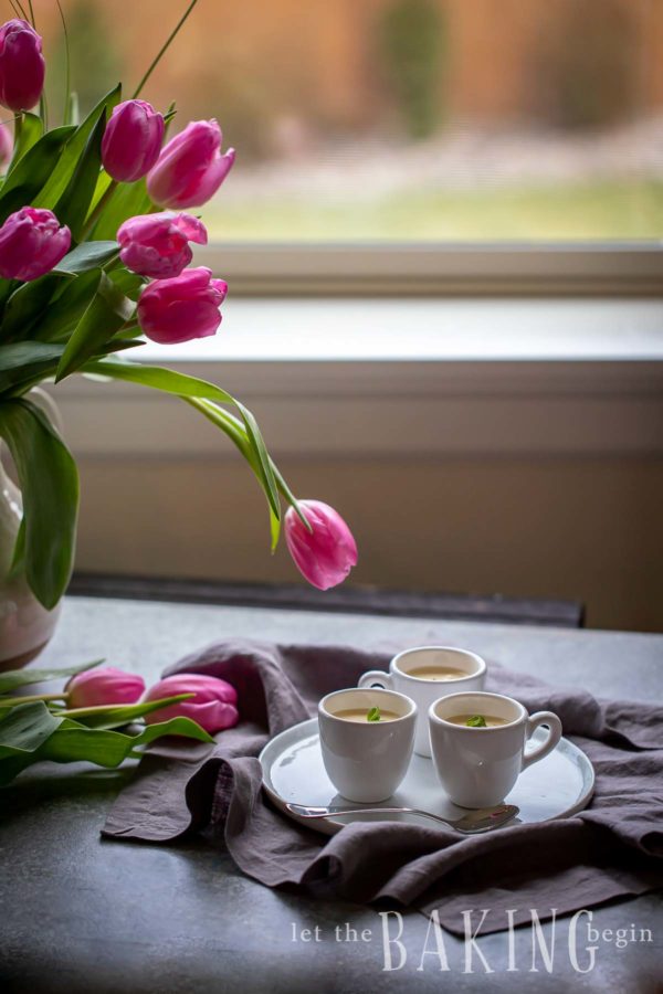Panna cotta recipe in 3 white mugs on a table with pink tulips next to it