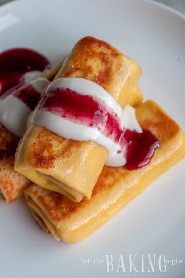 Stack of cheese blintz on a plate topped with a berry cream sauce