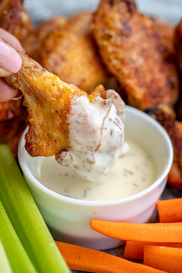 Baked chicken wings recipe being dipped into ranch with celery and carrots on the side.