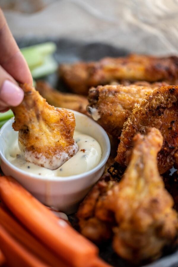 Ranch wing is being dipped into ranch, surrounded by more chicken wings and carrot sticks.