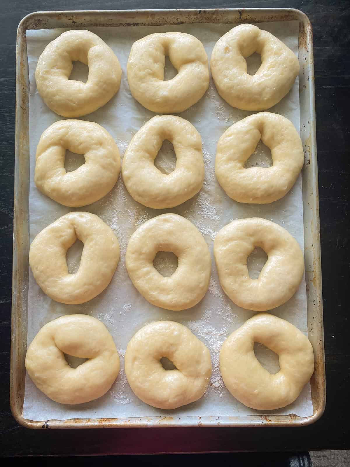 Twelve shaped bagels on a parchment lined baking sheet with wide open holes.