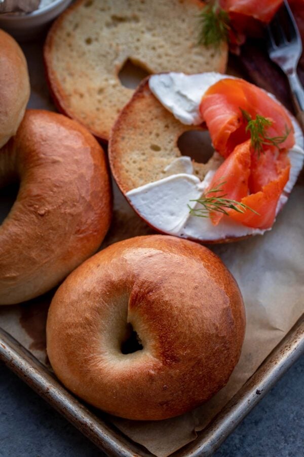 View of whole and cut bagels. The cut bagel is spread with cream cheese and lox or smoked salmon.