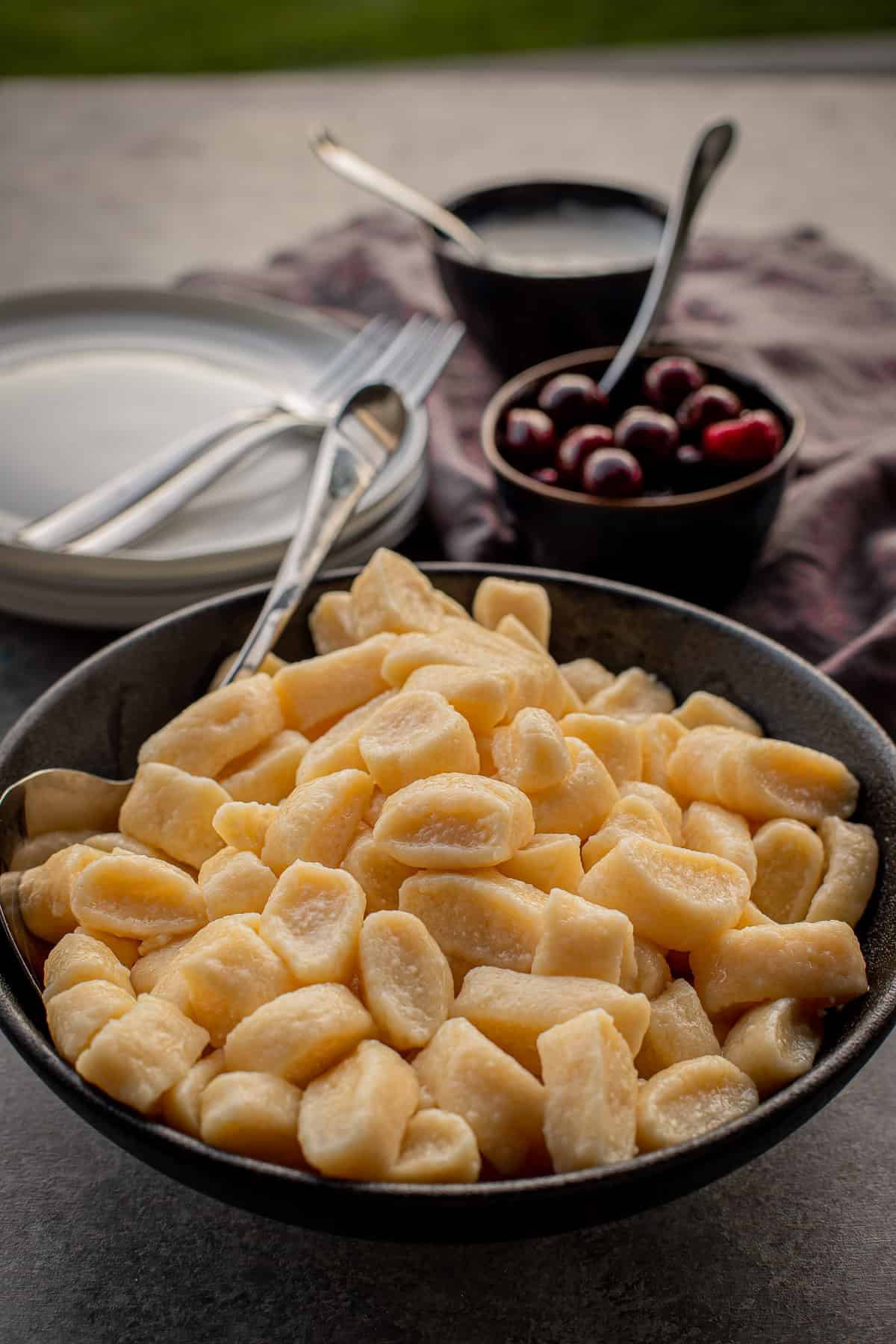 Lazy pierogies in a bowl, with cherries in a smaller bowl in the background, plates and forks.