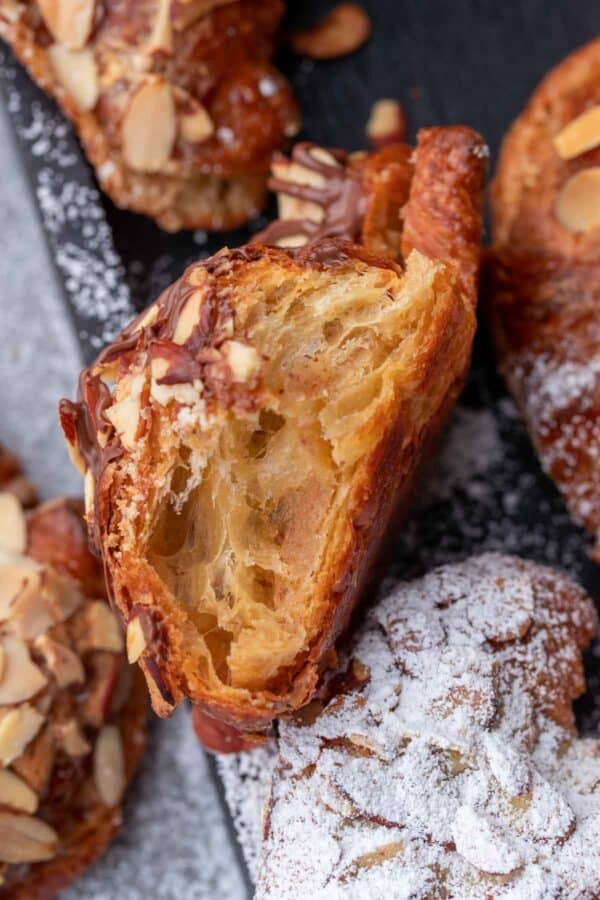 Almond croissant torn in half, exposing the inside of the croissant (the almond filling), surrounded by more croissants.