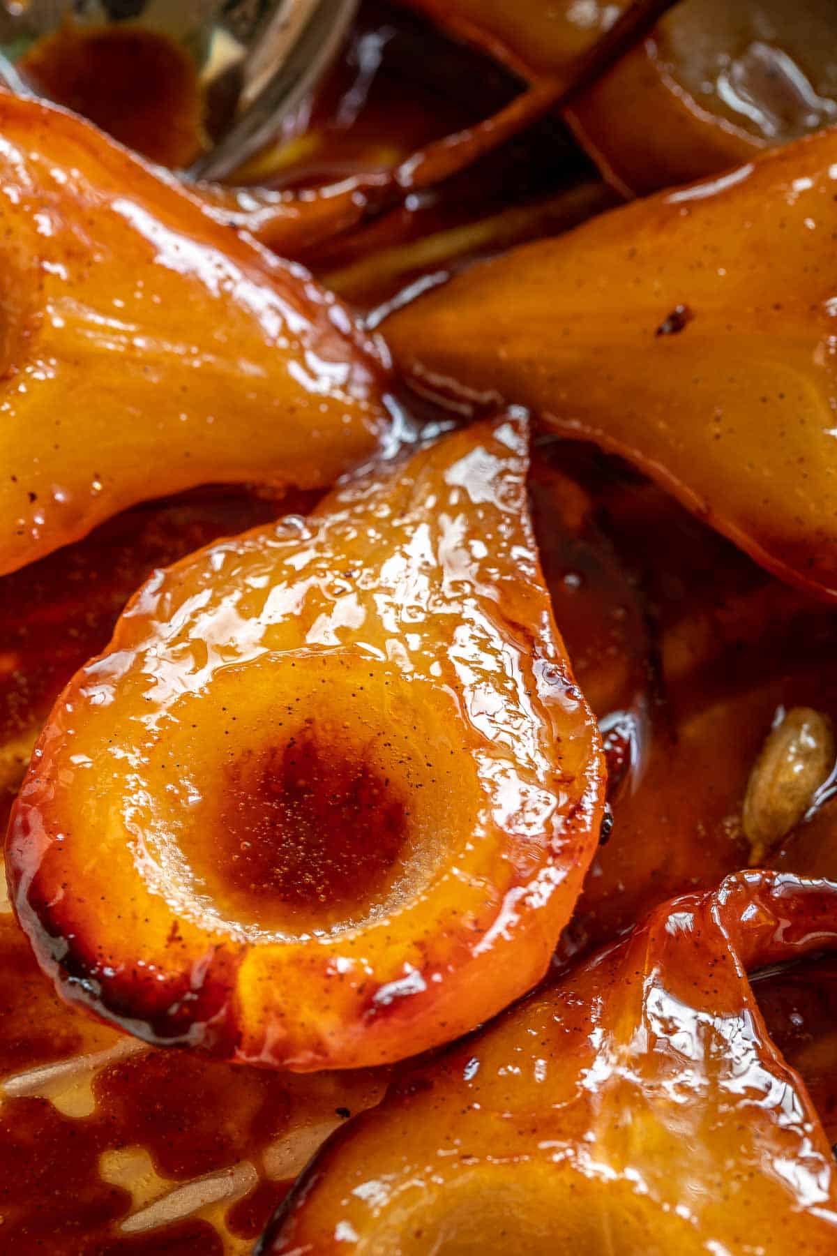 Caramelized pears in a dish, with caramel pooled around and in the pears, with vanilla beans speckled throughout.