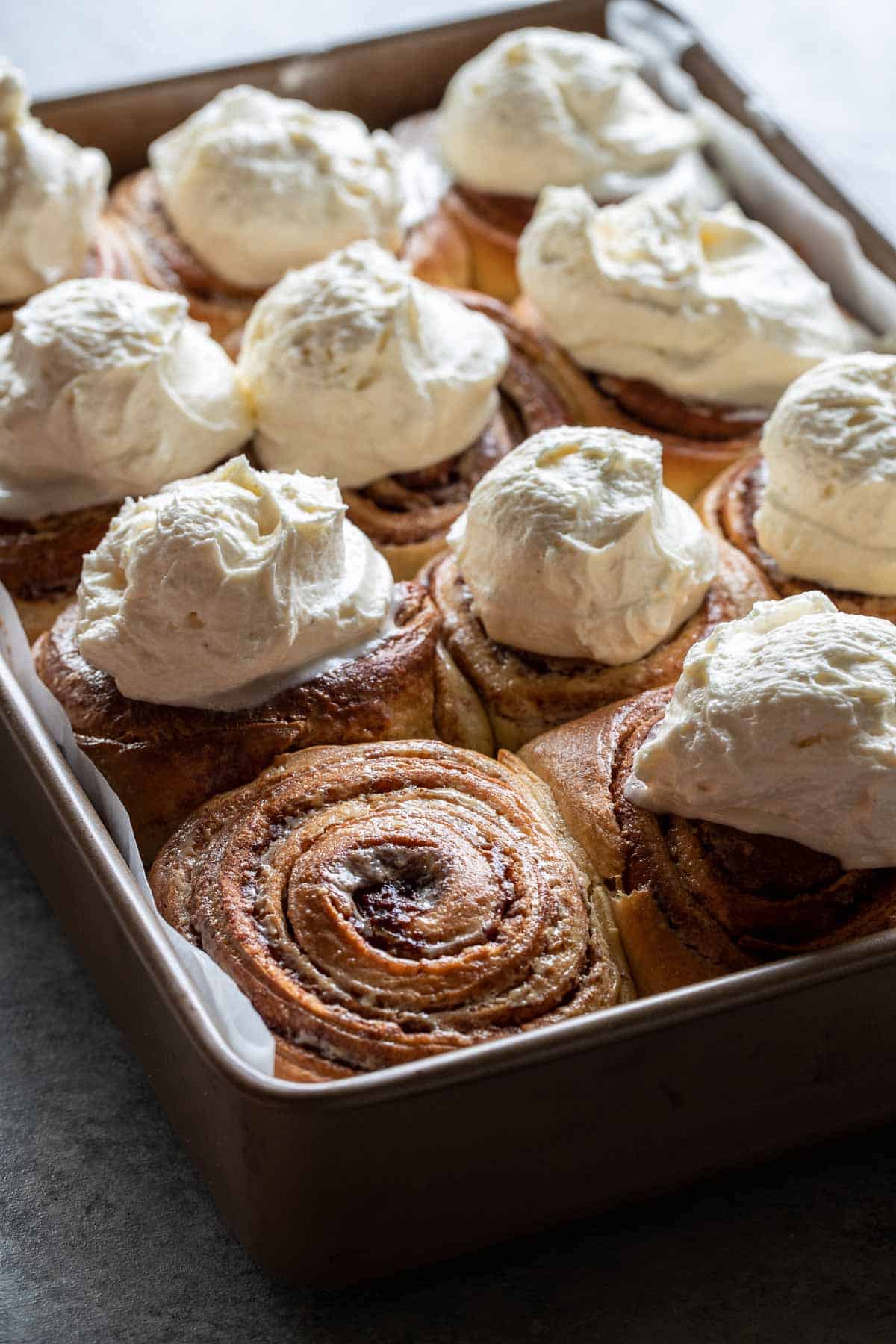 Cinnamon rolls in a pan with mounds of cream cheese icing over each roll.
