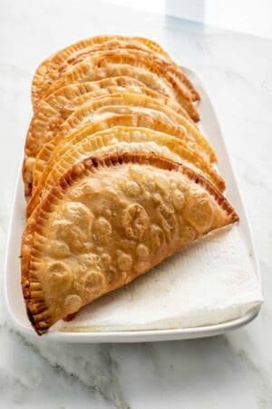 A bunch of chebureki lined up on a paper towel lined rectangle plate.