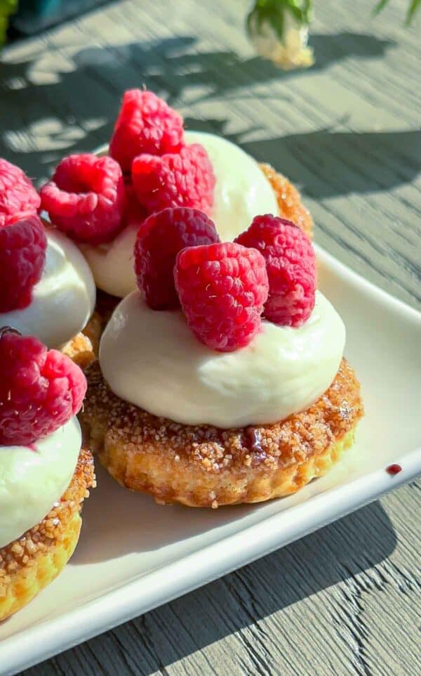 Puff pastry tarts filled with cheesecake filling and raspberries on top, sitting inside a white square plate.