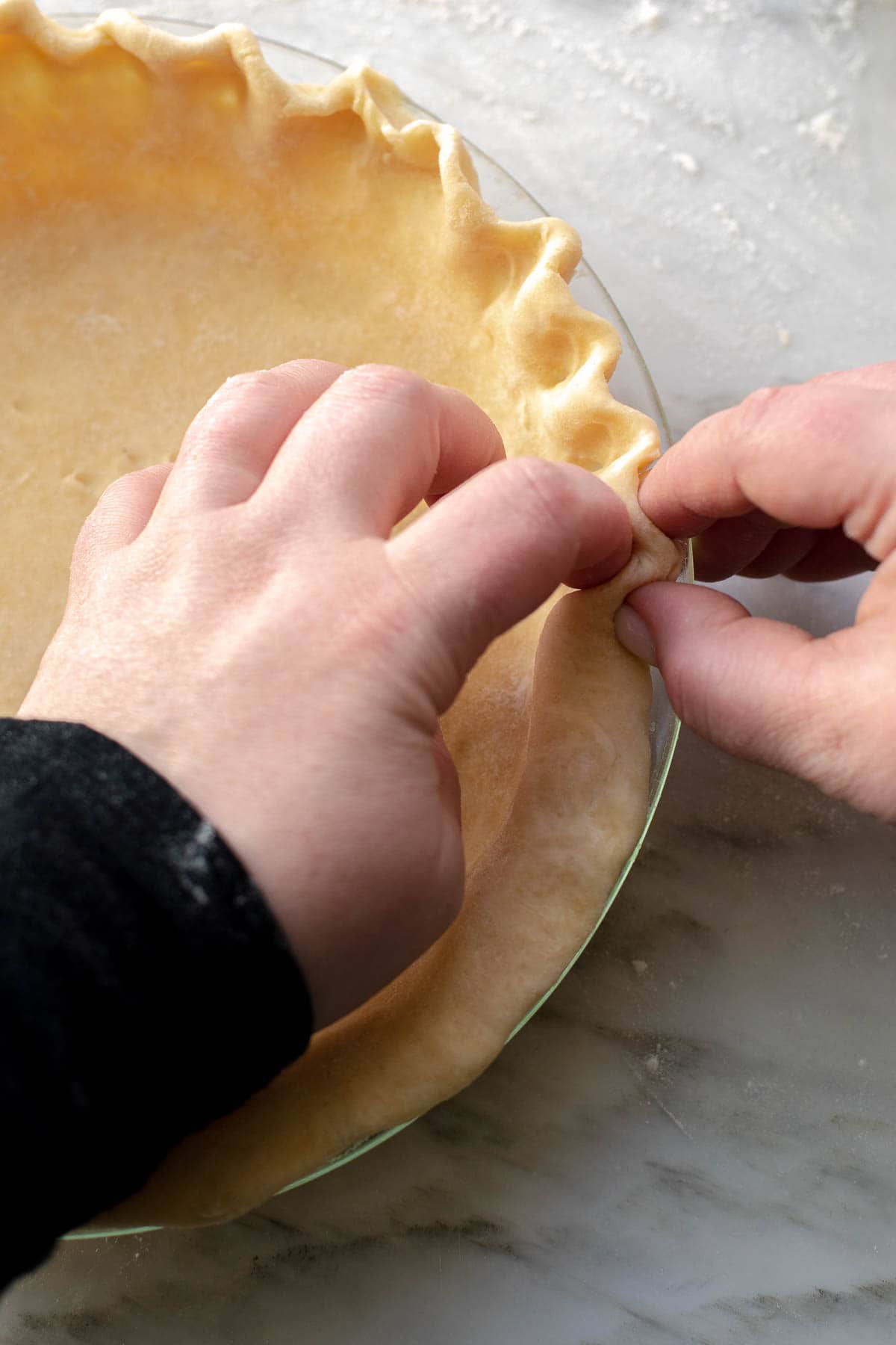 Close up of two hands making a fluted edge on a pie crust.