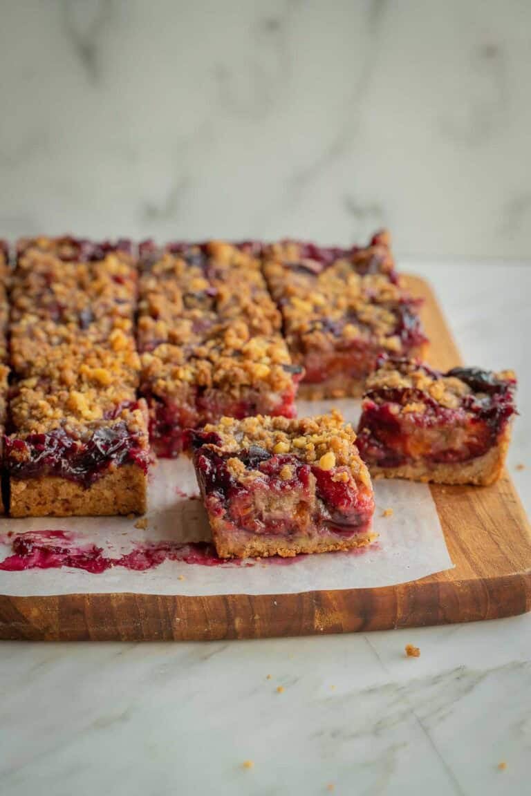 Squares of plum crumble bars on a wooden board lined with parchment paper