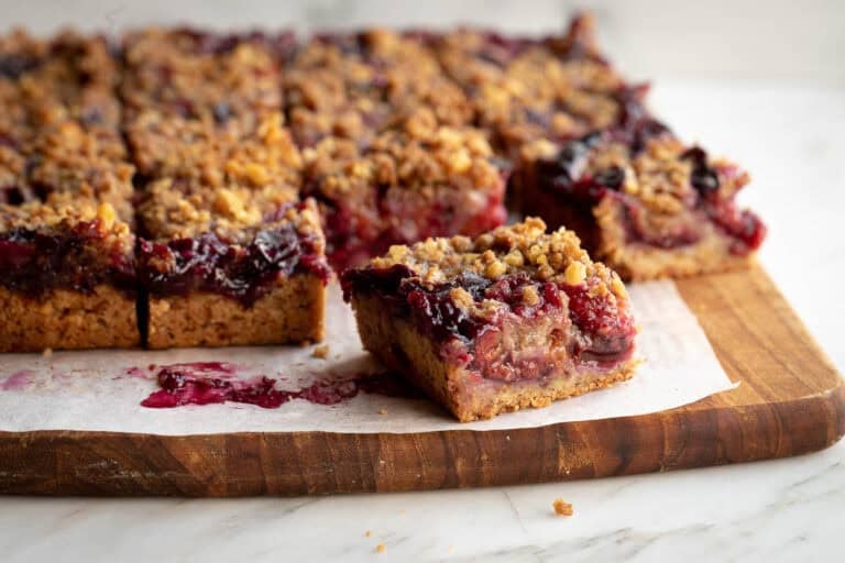 Plum crumble bars on a wooden board with one square pulled away from the slab