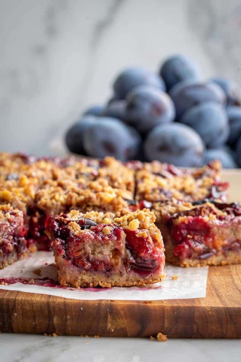 Plum crumble bars on a board with a bowl of fresh Italian prune plums behind them