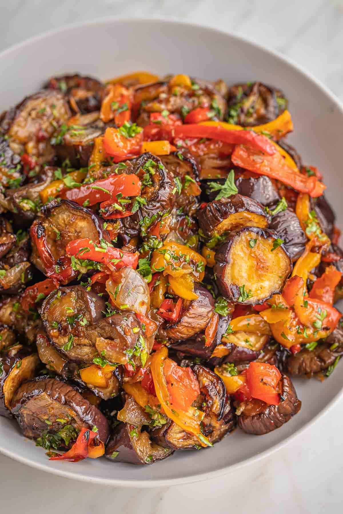 Close up of broiled eggplant rounds and charred red and orange pepper strips tossed with fresh parsley