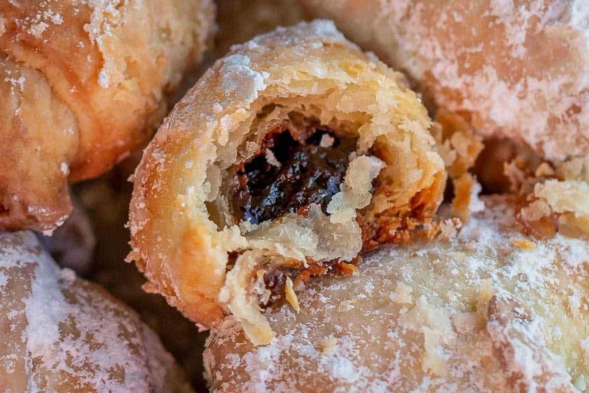 Rogaliki broken open showing thick prune plum butter filling inside flaky cream cheese pastry