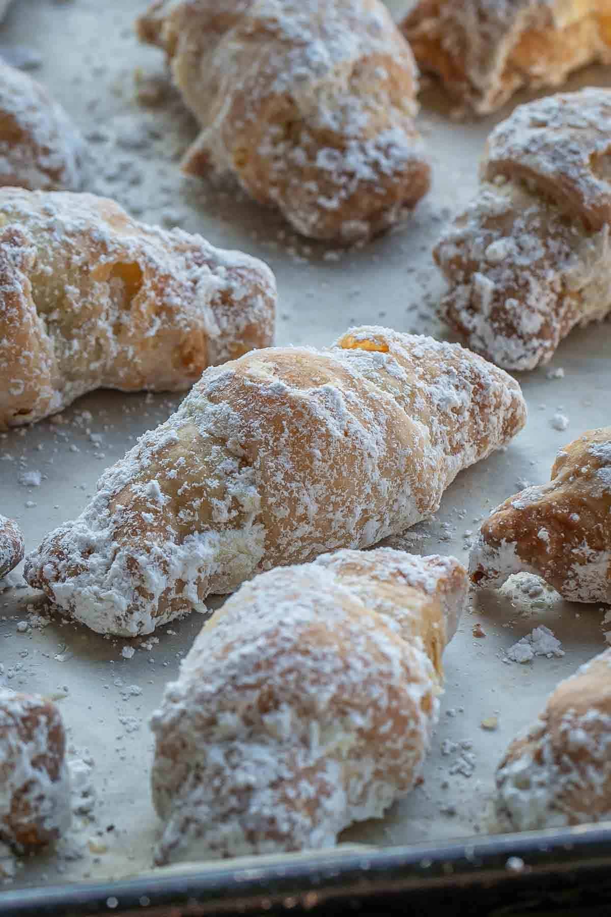 Rogaliki crescents coated in powdered sugar on a baking sheet