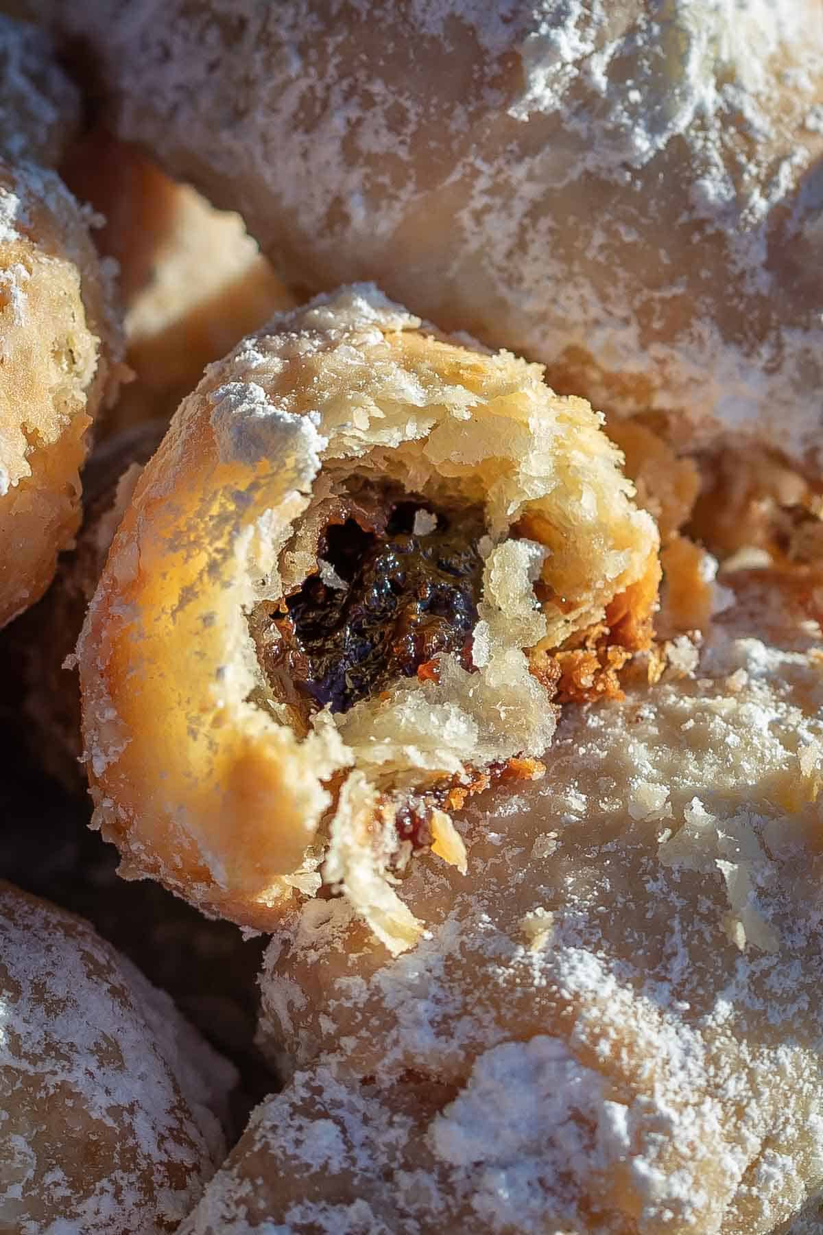 Close up of a rogalik broken in half showing dark plum butter filling against tender pastry