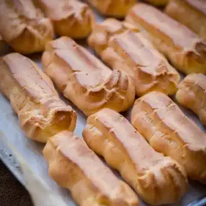 Baked choux pastry eclair shells, puffed and deep golden, on a parchment-lined baking sheet