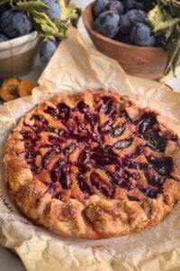 Italian plum galette with almond cream on parchment, surrounded by fresh Italian plums