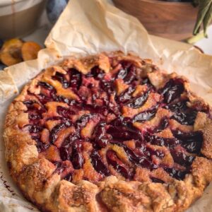 Italian plum galette with almond cream on parchment, surrounded by fresh Italian plums