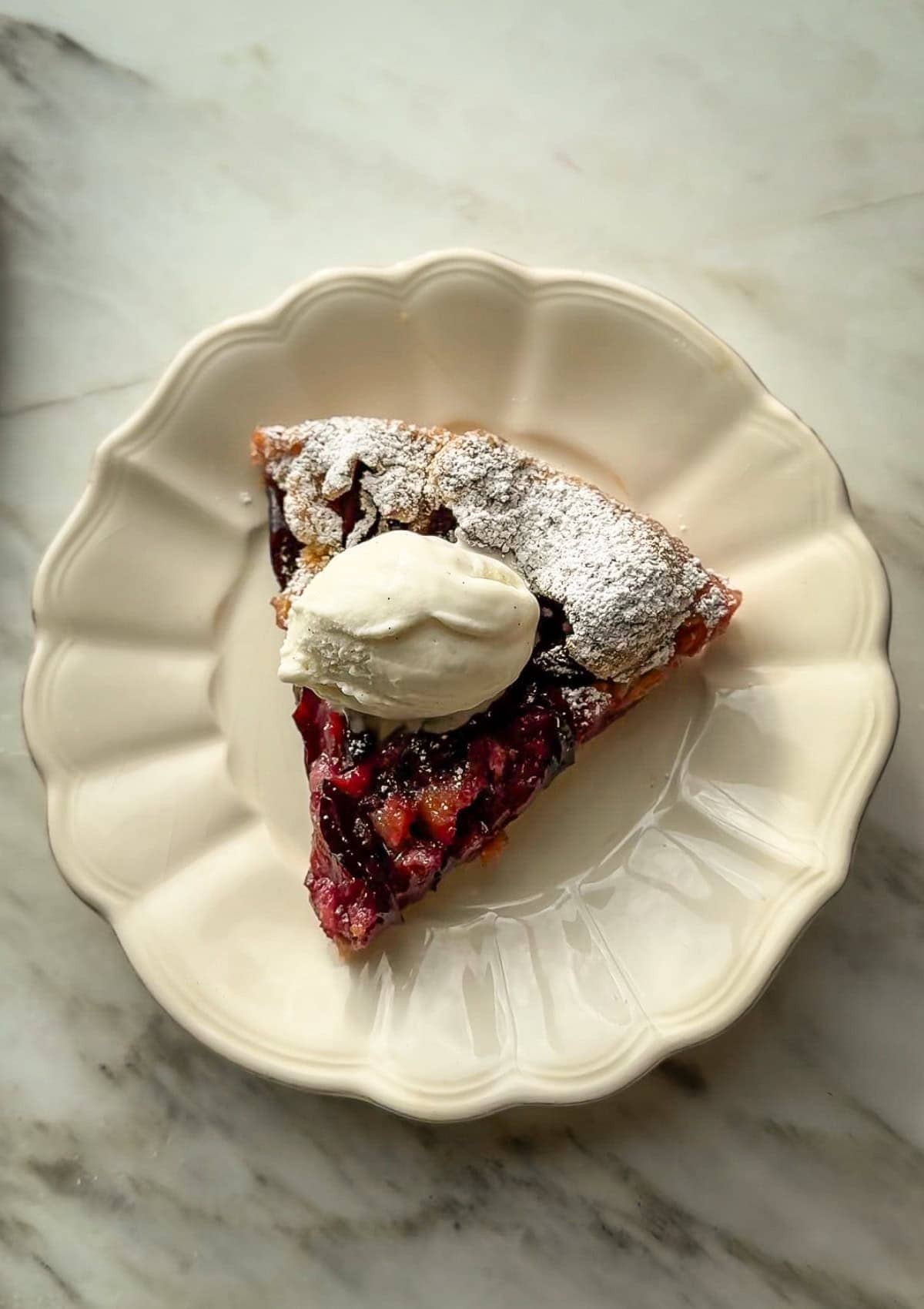 Overhead view of a plum galette slice on a plate with a scoop of ice cream