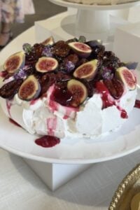 Roasted plum pavlova on a white cake stand with plum syrup running down the meringue