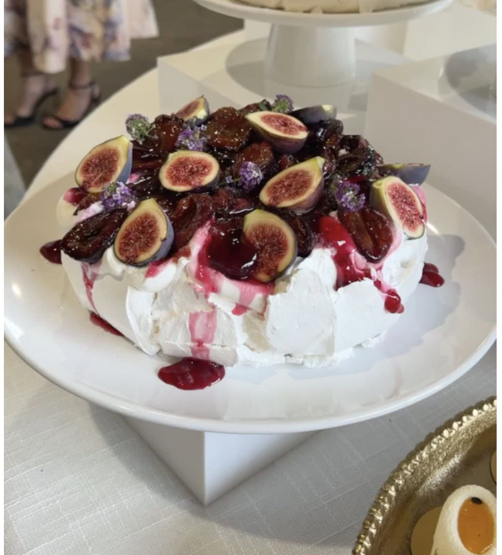 Roasted plum pavlova on a white cake stand with plum syrup running down the meringue