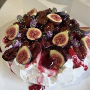 Roasted plum pavlova topped with caramelized plums, fresh figs and edible flowers