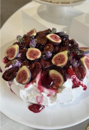 Roasted plum pavlova topped with caramelized plums, fresh figs and edible flowers