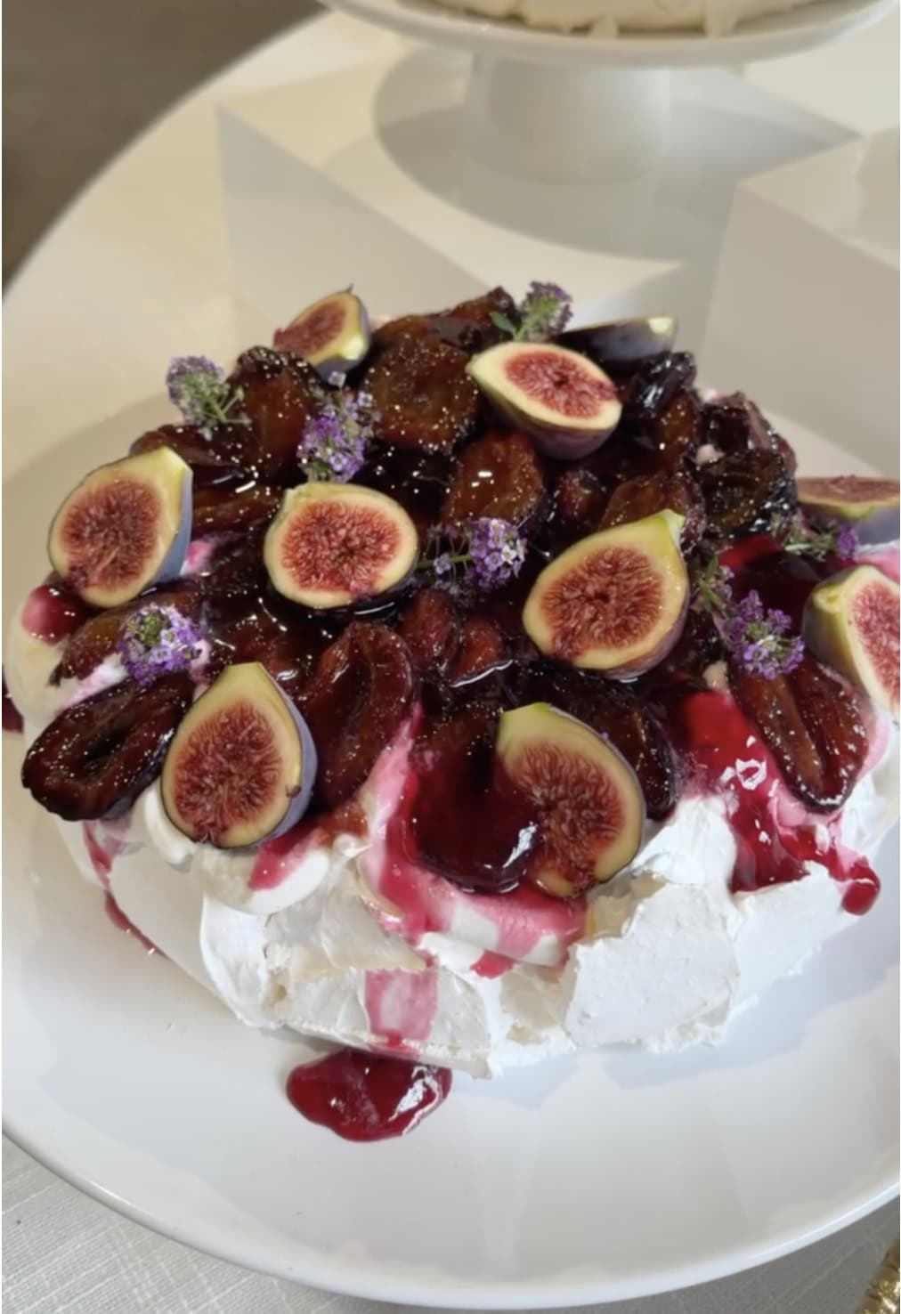 Roasted plum pavlova topped with caramelized plums, fresh figs and edible flowers