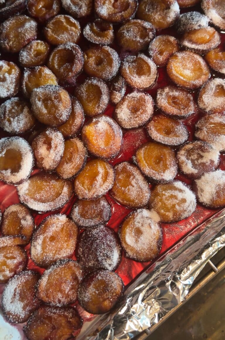 Italian prune plum halves cut side up on a baking sheet, sprinkled with sugar and sitting in their own juice