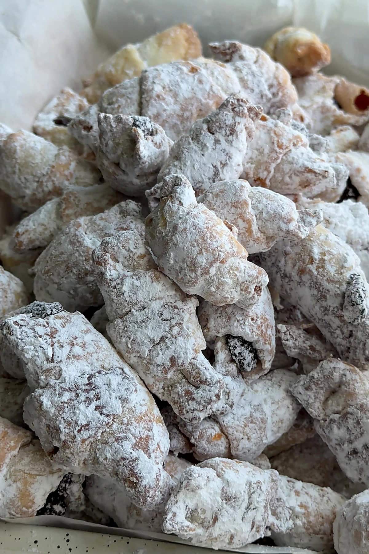 Rogaliki crescents buried in powdered sugar, piled in a parchment-lined box