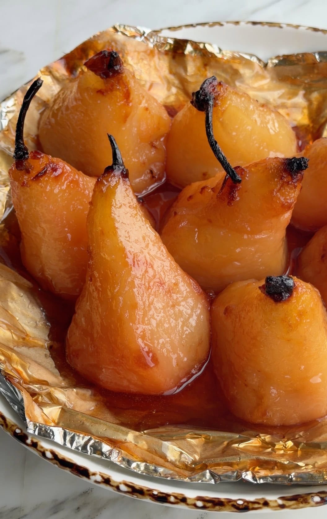 Whole roasted pears sitting in their caramel in a foil lined dish