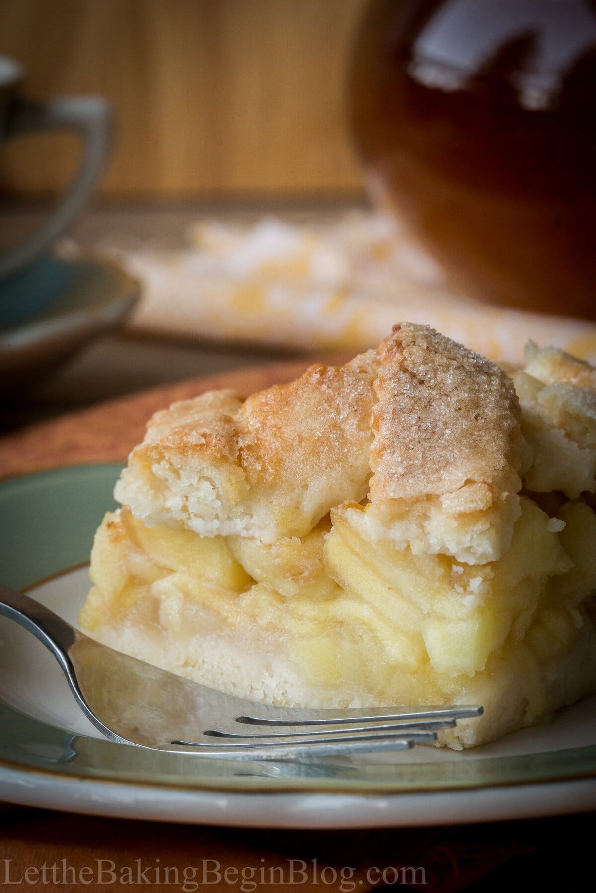 A slice of apple pirog on a green plate with a cup of tea behind it