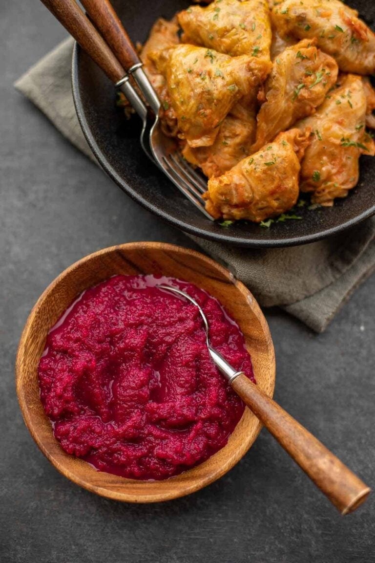 Wooden bowl of beet horseradish (cwikla) beside a plate of cabbage rolls