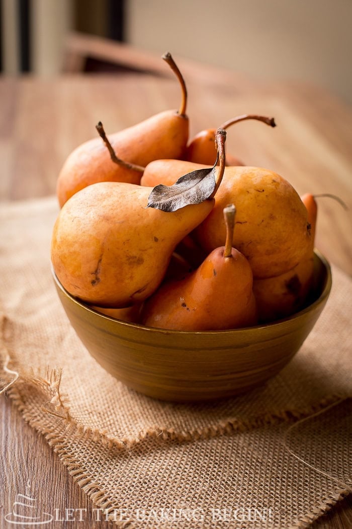 Whole Bosc pears for poaching with stems on, in a bowl on burlap