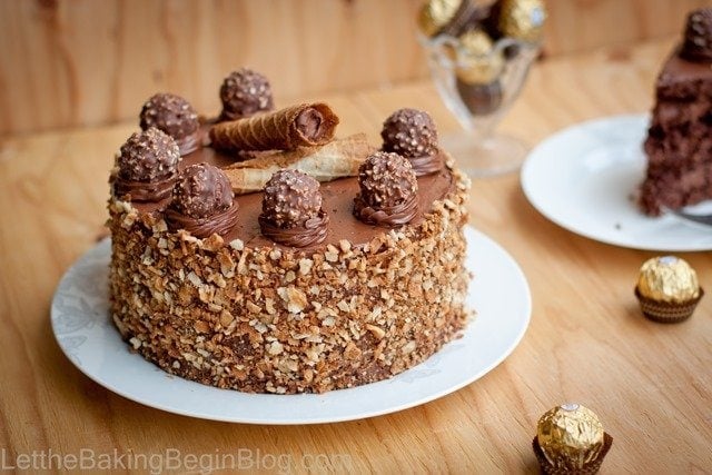 Ferrero Rocher cake on a white plate with crushed wafers pressed onto the sides and Ferrero Rocher candies on top