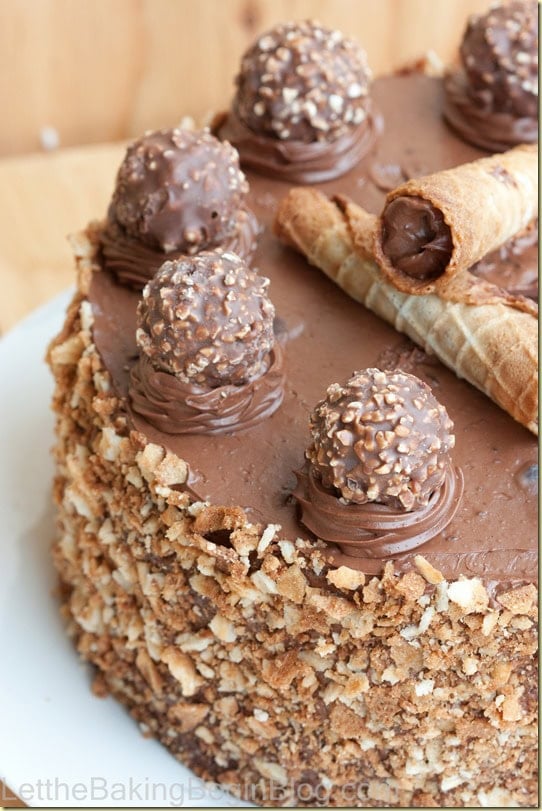 Top of a Ferrero Rocher cake with piped Nutella buttercream stars, a Ferrero Rocher on each, rolled wafers and crushed wafers on the sides