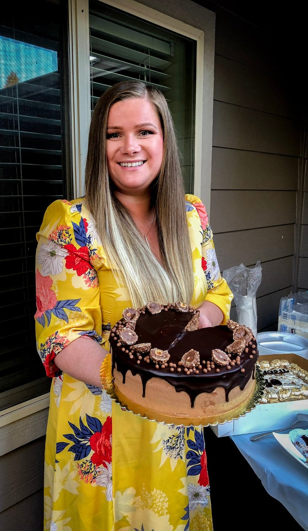 Marina, the author behind Let the Baking Begin, holding a Ferrero Rocher cake with a chocolate drip and Ferrero Rocher candies on top