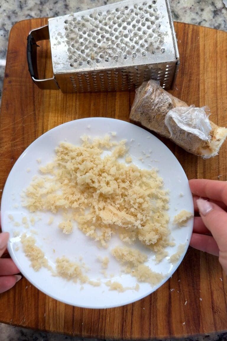Freshly grated horseradish root on a plate next to a box grater