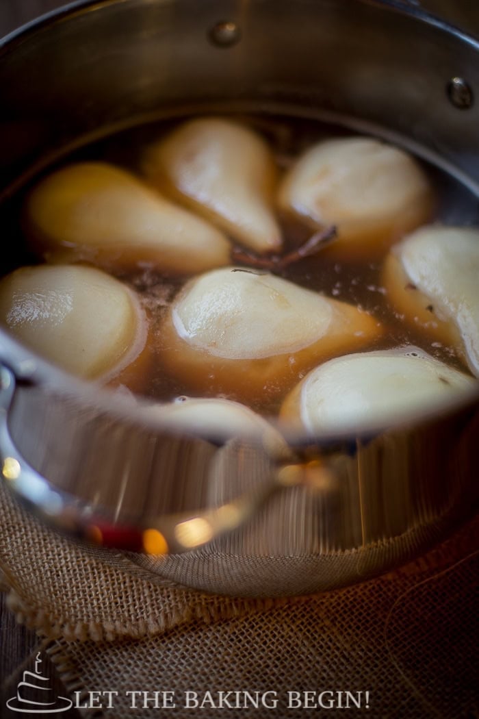Poached pears soaking in amaretto syrup in the pot, ready to make ahead