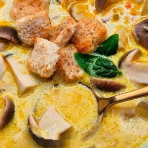 Spoonful of creamy porcini mushroom soup in a bowl with croutons and basil