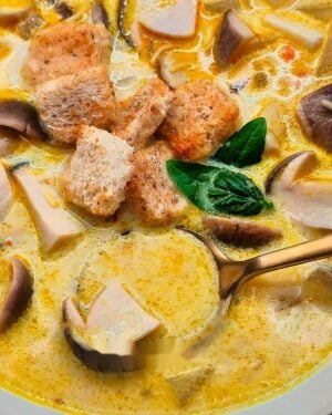 Spoonful of creamy porcini mushroom soup in a bowl with croutons and basil